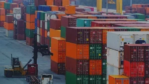 A busy container yard with tall stacks of colorful shipping containers and a reach stacker moving a container, representing LCL shipping from China to the USA.