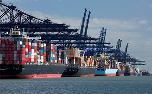 A row of large container ships loaded with colorful shipping containers docked at a port under massive blue gantry cranes.